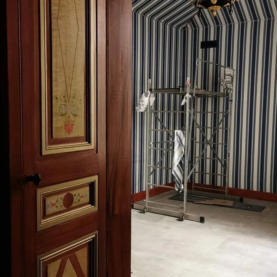 Détail d'une porte peinte en faux bois à losanges devant un mur rayé